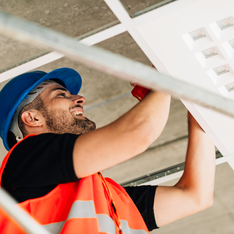 A person in a hard hat and vest working on a ceiling

Description automatically generated