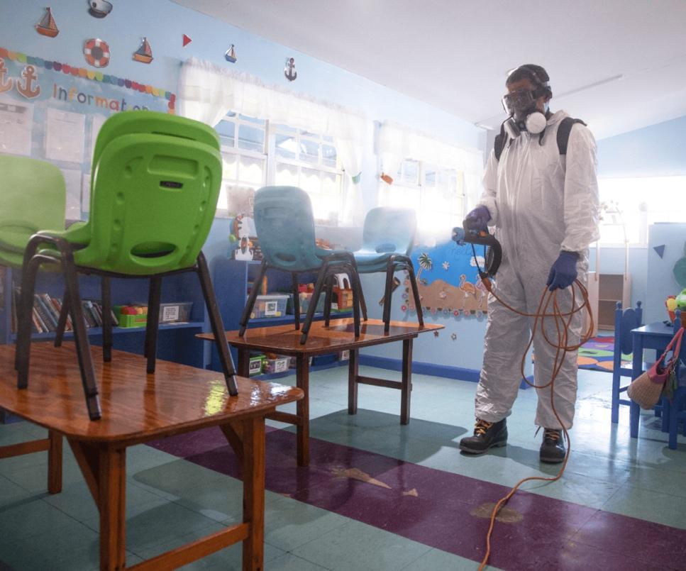 A person in a white suit and mask spraying chairs

Description automatically generated